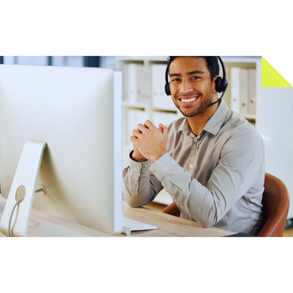 A smiling person wearing a headset sits at a desk with a large computer monitor, perhaps coordinating freight services for RDT Enterprises. Their hands are clasped as they work in an office setting with shelves in the background, exuding professionalism and efficiency.