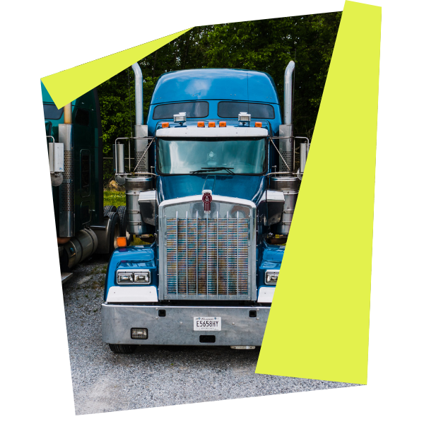Front view of a blue semi-truck with chrome accents, branded by RDT Enterprises, parked on a gravel surface. It features a large grille and visible exhaust pipes, set against a backdrop of trees. The image is tilted with a yellow border.